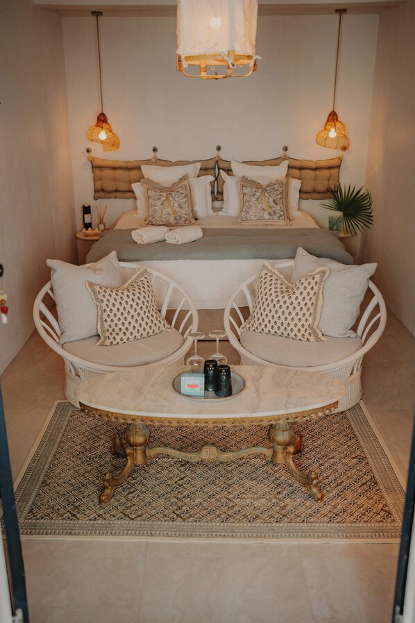 A bedroom with two white wicker chairs, a small round table, and a bed with multiple pillows.