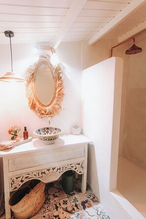 A bathroom with a white vanity, a mirror with a fringe, a hanging light, a patterned bowl, and a shower area. - Bleu guesthouse (Saint-François)