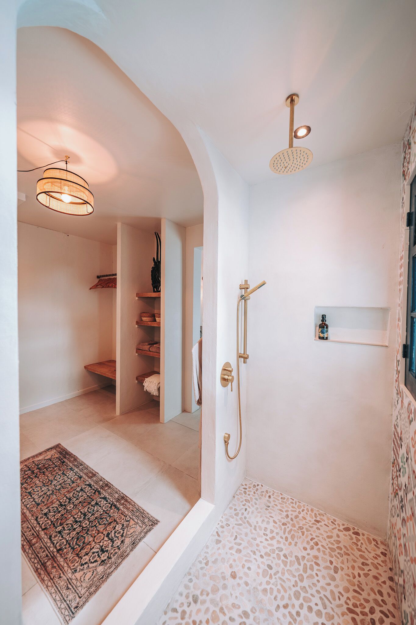 A walk-in closet with shelves and a hanging rack, a shower with a handheld showerhead, and a patterned rug on the floor.