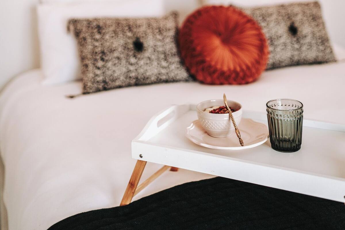 A bed with white bedding, a tray with a cup and a bowl, and two framed pictures on the wall.