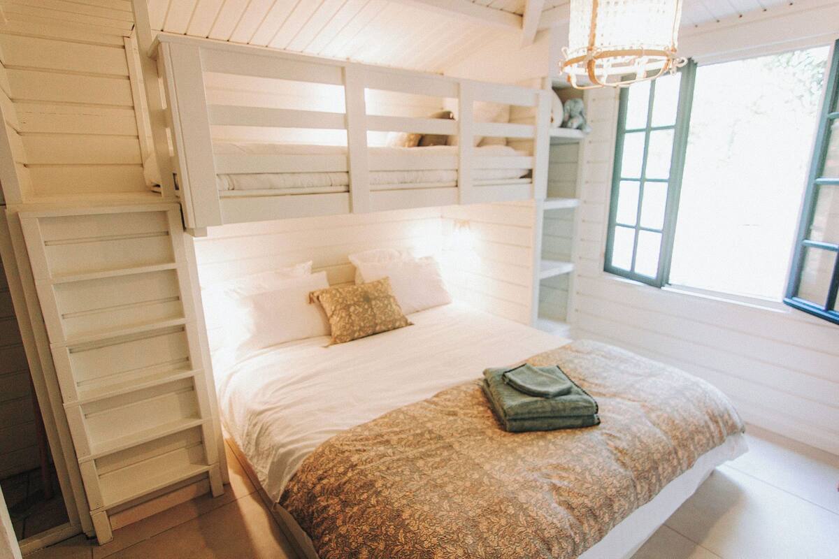 A bunk bed with a ladder, a window with a view, and a bedside table with a lamp.