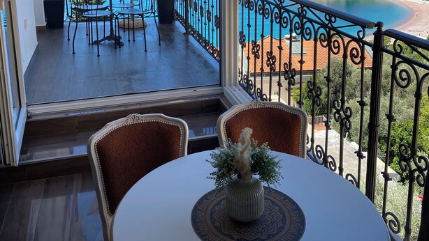 A balcony with a table and chairs, a potted plant, and a view of the sea and a coastal town. - Sveti Stefan Panorama View Apartment (Sveti Stefan)