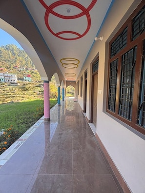 A corridor with a tiled floor, a series of windows on one side, and a view of a hillside with buildings in the background.