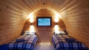 A cozy attic bedroom with two beds, a television, and wall-mounted lights. - Glamping Pod - Glendalough (Laragh)