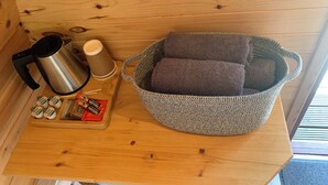 A wooden cabin interior with a metal kettle, a woven basket with cushions, and a wooden shelf with various items. - Glamping Pod - Glendalough (Laragh)