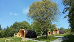 Two wooden cabins with arched doorways, surrounded by lush greenery and a clear sky. - Glamping Pod - Glendalough (Laragh)