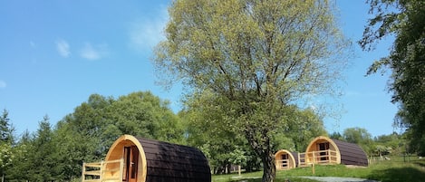 Two wooden cabins with arched doorways, surrounded by lush greenery and a clear sky.