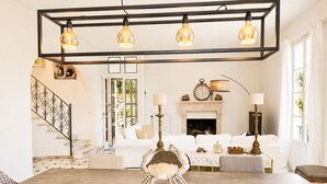 Ein großzügiger Wohnraum mit einem großen Tisch, weißen Sofas, einem Kamin und einer Treppe.