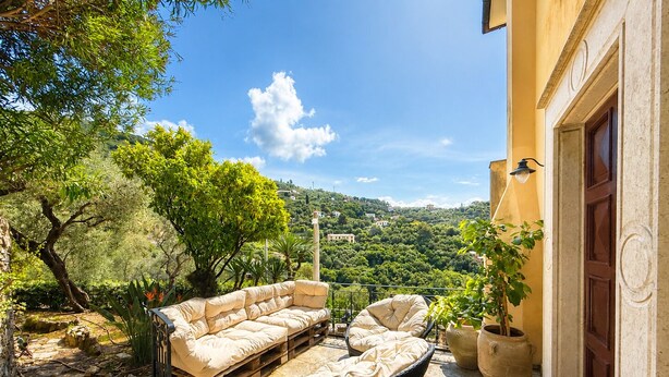 Eine Terrasse mit Gartenmöbeln, eine Steintreppe und Blick auf eine Hügellandschaft.