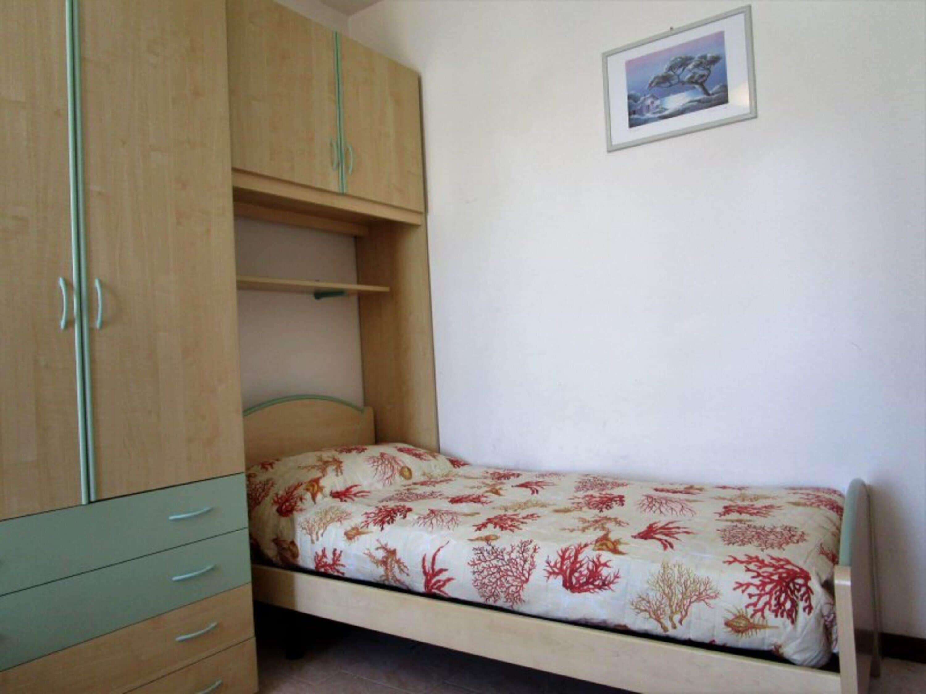 A single bed with a floral bedspread, a wooden wardrobe with multiple drawers, and a framed picture on the wall.