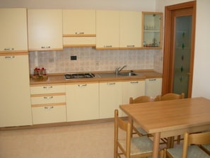 Eine Küche mit beigen Schränken, einer Holz Arbeitsplatte, einem Spülbecken und einem Esstisch mit Stühlen.