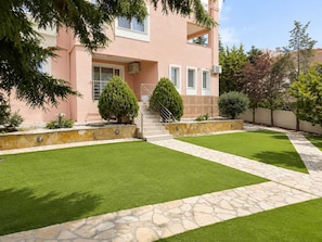 A pink building with a stone staircase leading to a door, surrounded by well-maintained lawns and trees. - Treasure B&B - Garden Stay in Paloukia Salamina (Paloukia)