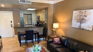 A living room with a leather sofa, a coffee table with flowers, a dining area with chairs, and a kitchen in the background. - Entire Condo just a short walk from the Strip! (Las Vegas)
