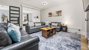 A modern living room with a sofa, coffee table, and a painting on the wall. - The Skylight Vault - Bright Downtown Loft Living/Pet Friendly/Short Walk to Shop (Sarnia)