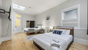 A bedroom with a large bed, a smaller bed, a desk, and a chair. - The Skylight Vault - Bright Downtown Loft Living/Pet Friendly/Short Walk to Shop (Sarnia)