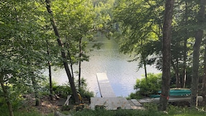 Blick auf einen See mit einer Holzsteganlage, umgeben von üppiger Vegetation und Bäumen.