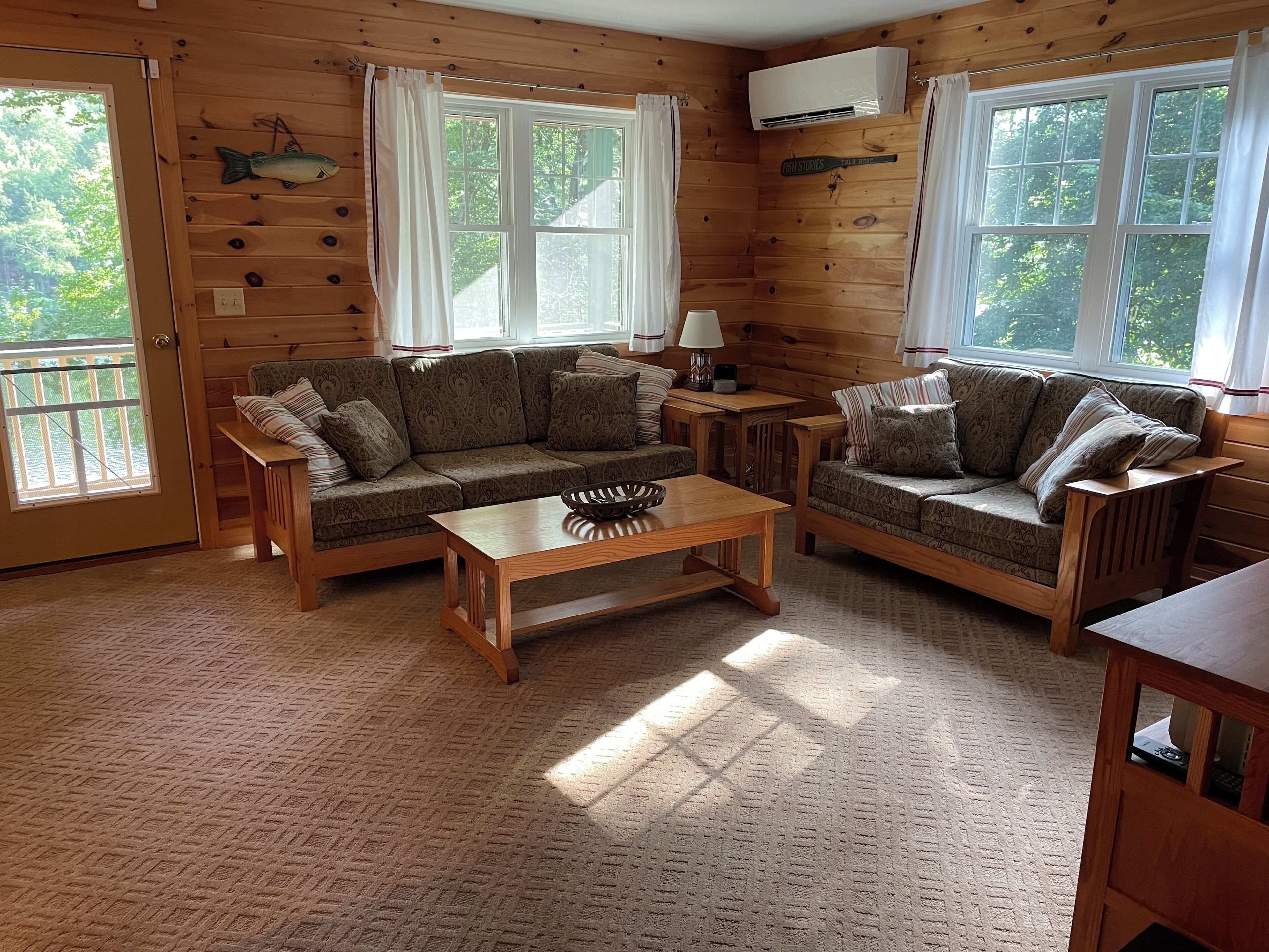 Un intérieur de chalet chaleureux avec des murs en bois, deux canapés, une table basse et de grandes fenêtres.