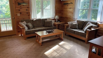 Un intérieur de chalet chaleureux avec des murs en bois, deux canapés, une table basse et de grandes fenêtres.