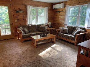 Un intérieur de chalet chaleureux avec des murs en bois, deux canapés, une table basse et de grandes fenêtres.