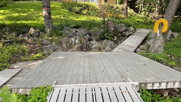 Une terrasse en bois menant à une maison dotée d’un balcon, le tout entouré de verdure et de rochers.