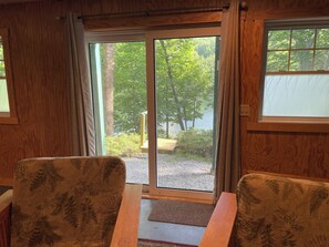 Une pi èce au décor intérieur en bois, avec une porte-fenêtre coulissante donnant sur un espace extérieur agrémenté d’arbres et d’un banc.