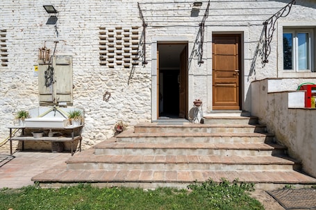 Un bâtiment en pierre avec une porte en bois, des marches menant à l’entrée et un petit espace extérieur comprenant une table et des plantes.. Chambre Ghibellina à La Campana d'Oro, au cœur du Casentino