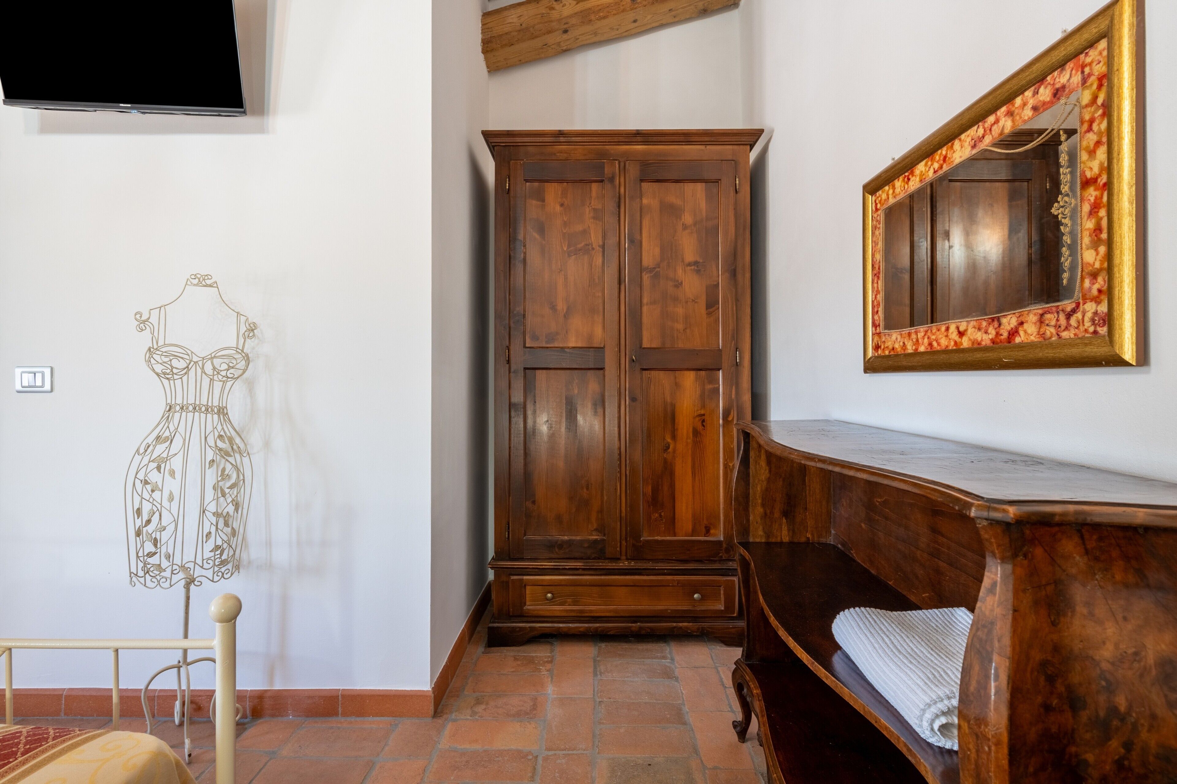 A room with a wooden wardrobe, a mirror with a floral frame, and a bed with a headboard.