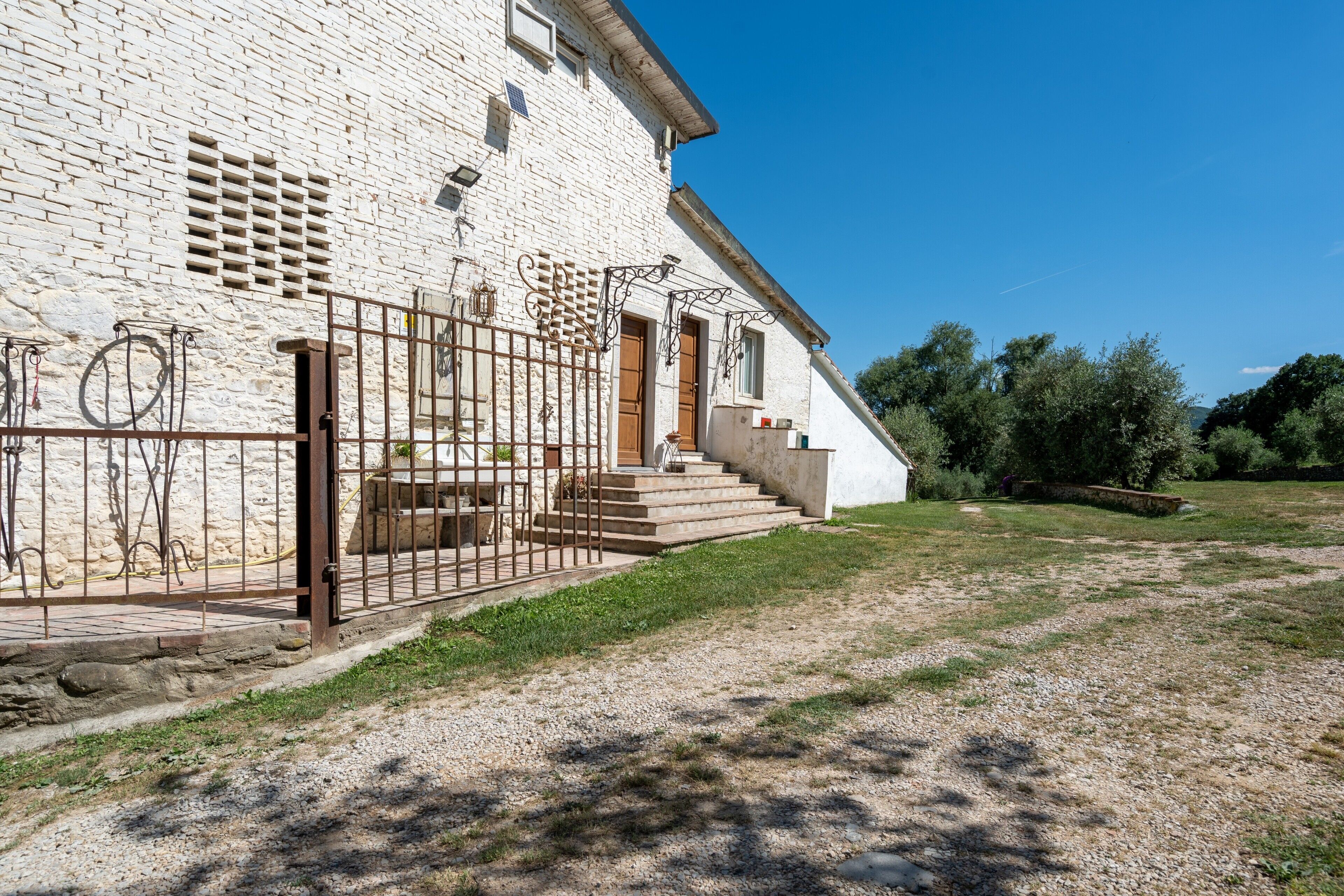 A white brick building with a gated entrance, steps leading to a door, and a gravel path.