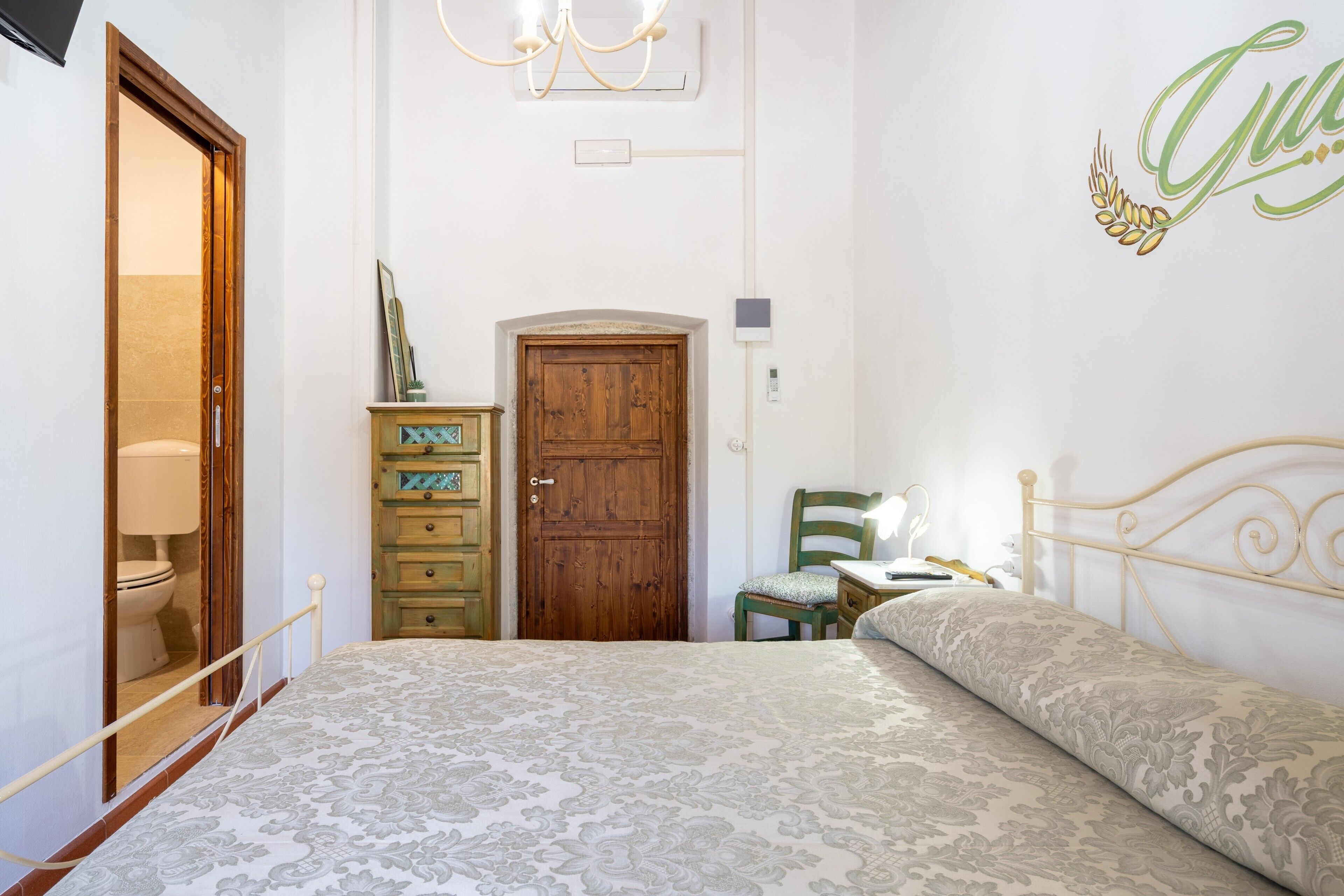 Una camera da letto con un letto, una porta in legno, una cassettiera, una sedia e una parete con un fregio decorativo.
