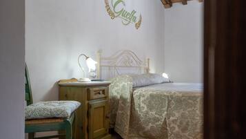 Un dormitori amb un llit, una tauleta de nit amb una làmpada, una cadira i una paret amb una decoració amb un nom.