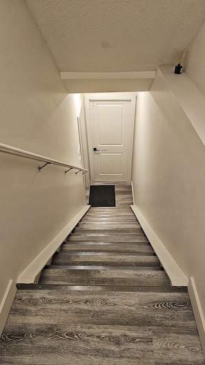Eine Holztreppe mit einer weißen Tür oben, einer Handlauf links und einer Fußmatte unten.