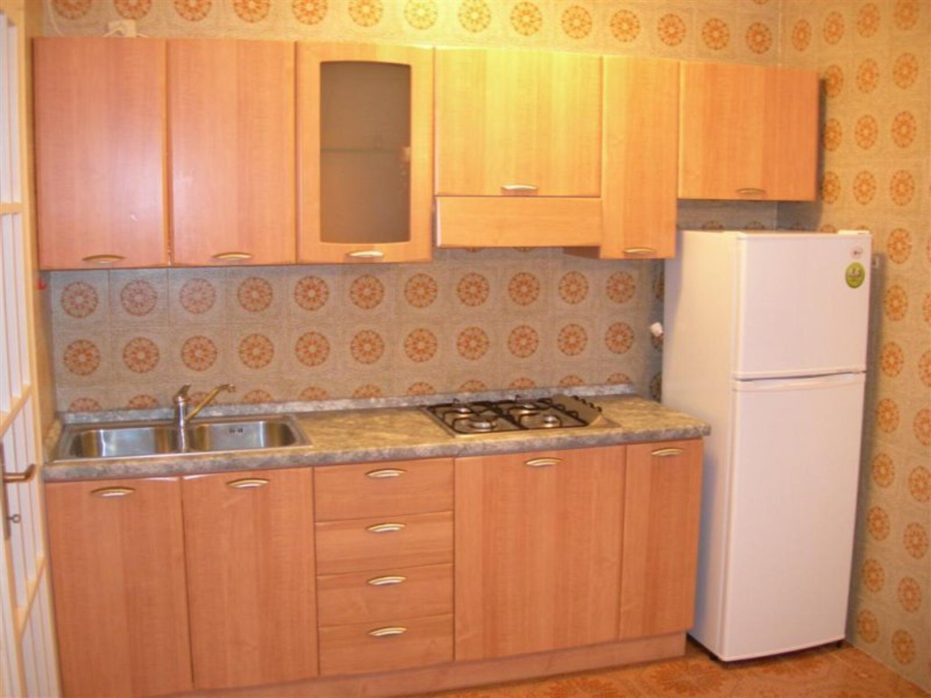 Une cuisine avec des meubles de rangement en bois, un évier, une cuisinière et un réfrigérateur blanc.