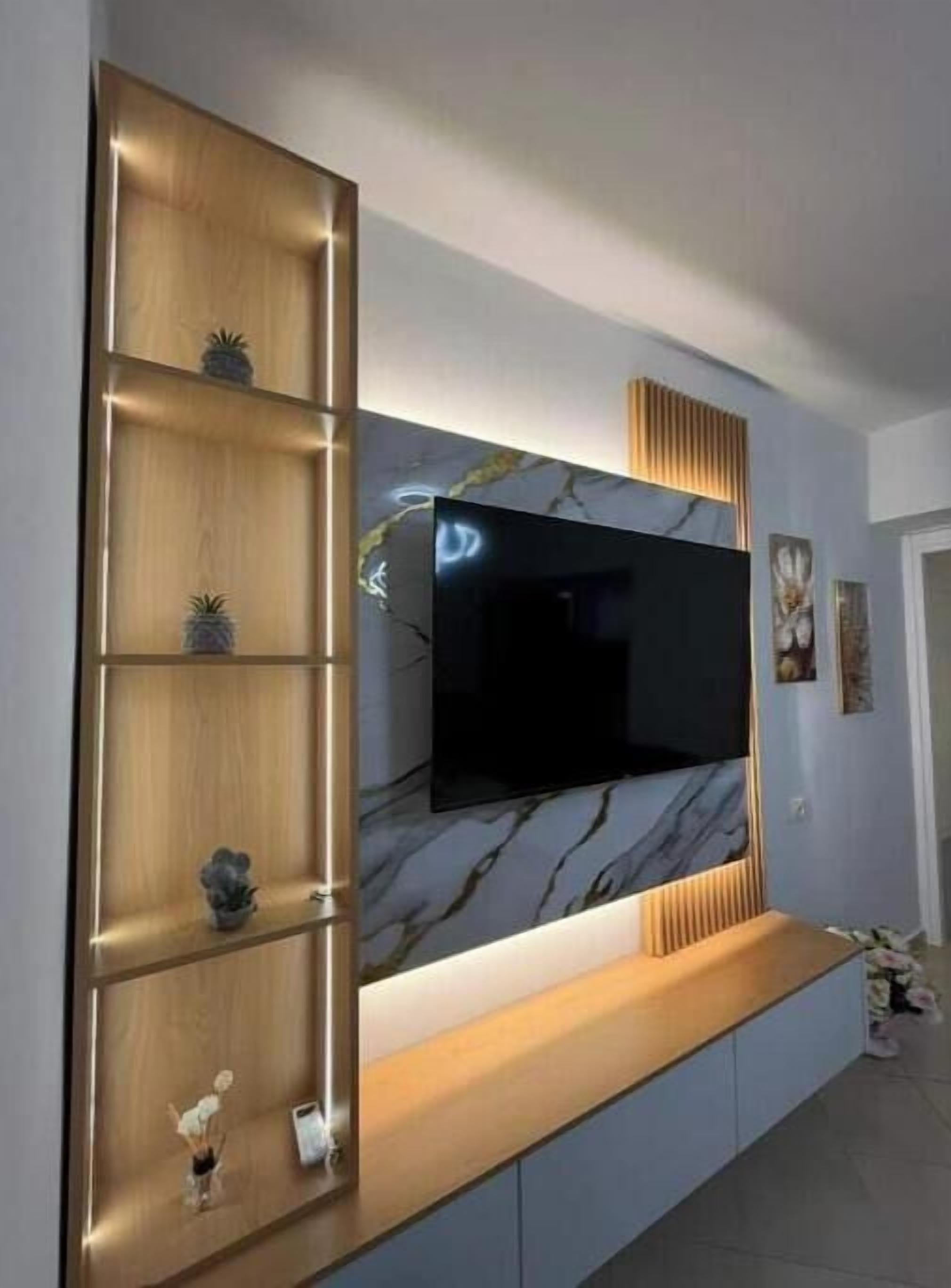 Un moderno salón con un televisor de pantalla plana grande montado en una pared con diseño que imita el mármol. Hay estanterías de madera con objetos decorativos y una consola de madera debajo del televisor.