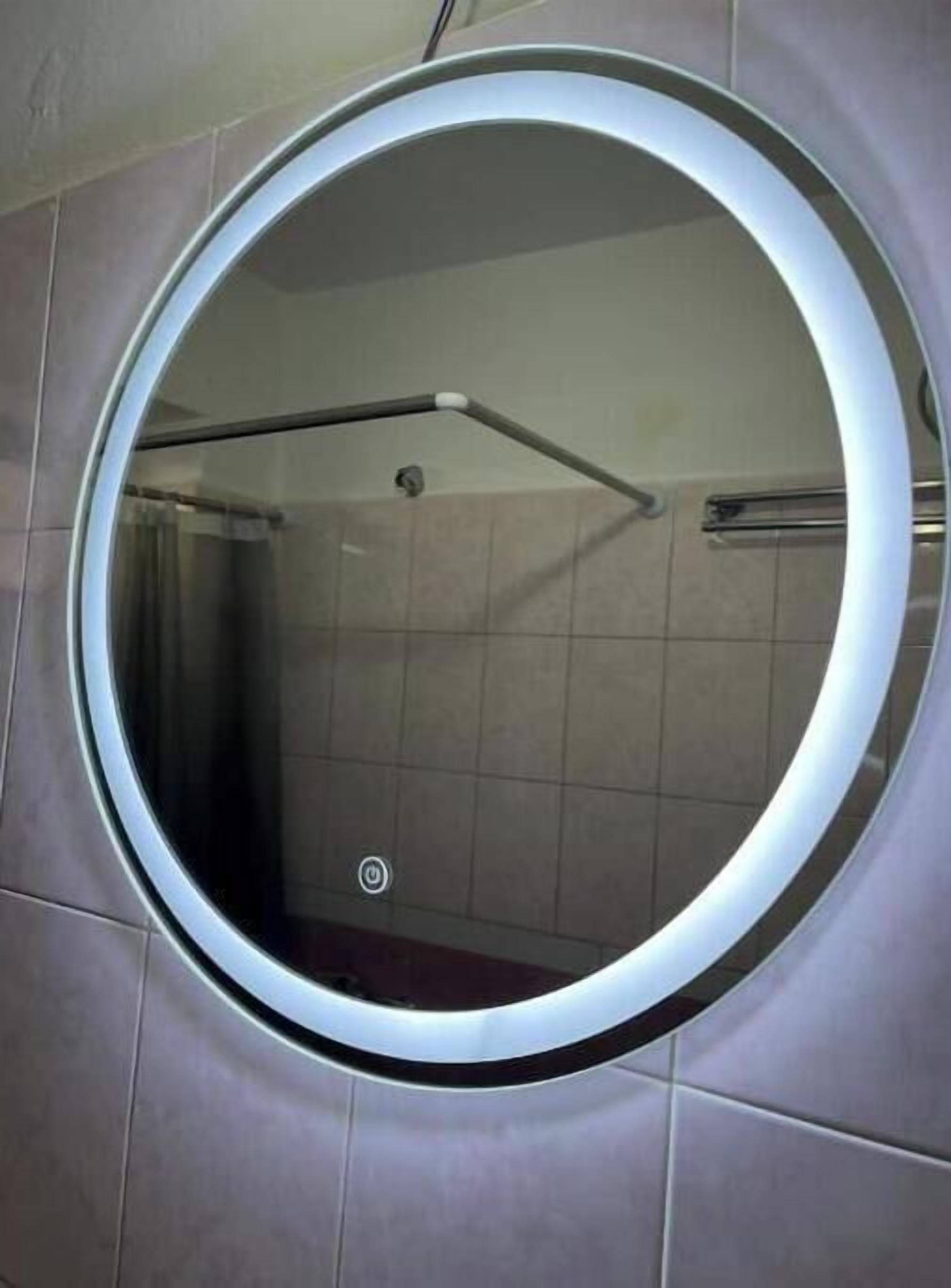 Un miroir rond, doté d’un cadre métallique, fixé sur un mur recouvert de carreaux.