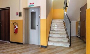 A staircase with a handrail, a fire extinguisher mounted on the wall, and a door with a sign above it. - Hostdomus - Seaside (Noli)
