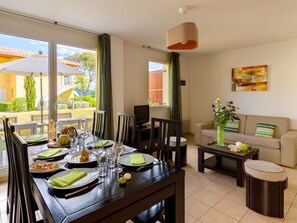 Un comedor con una mesa dispuesta para cuatro, un sofá, un televisor y una ventana con cortinas.