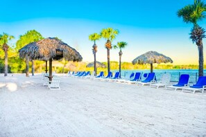 A beach with thatched umbrellas, white lounge chairs, and palm trees. - Disney-Welcome Home- Retreat w/ Pools & Lake Views (Davenport)