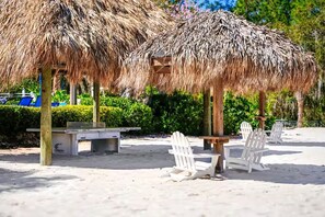 A beach area with thatched umbrellas, white Adirondack chairs, and a concrete bench. - Disney-Welcome Home- Retreat w/ Pools & Lake Views (Davenport)