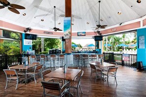 An outdoor restaurant with wooden tables and chairs, ceiling fans, and a view of the beach. - Disney-Welcome Home- Retreat w/ Pools & Lake Views (Davenport)