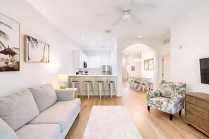 A modern living space with a sofa, a patterned armchair, a wooden cabinet, and a kitchen area with bar stools. - Disney-Welcome Home- Retreat w/ Pools & Lake Views (Davenport)