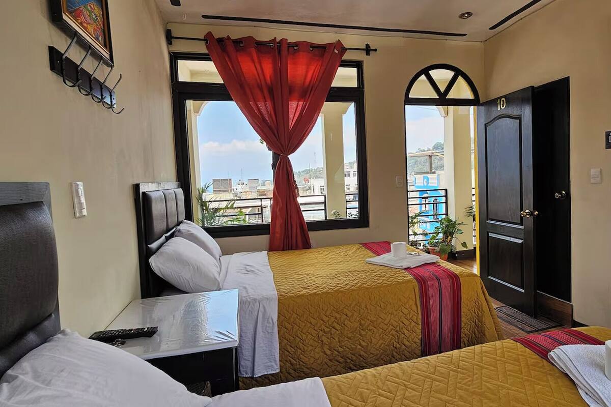 A hotel room with two beds, a TV, a window with a red curtain, and a door marked with the number 10.