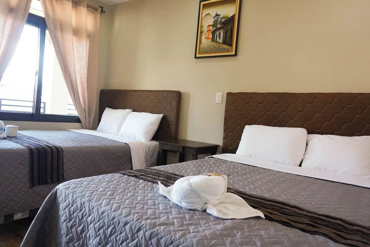 Two twin beds with headboards, a painting on the wall, and a window with curtains.