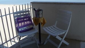 A balcony with a white chair, a small table with a yellow cloth, and a purple bag labeled 'Hotel Supreim'. - Hotel Suprem sul Mare (Rimini)