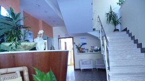 A reception area with a reception desk, chairs, a staircase, and potted plants. - Hotel Suprem sul Mare (Rimini)