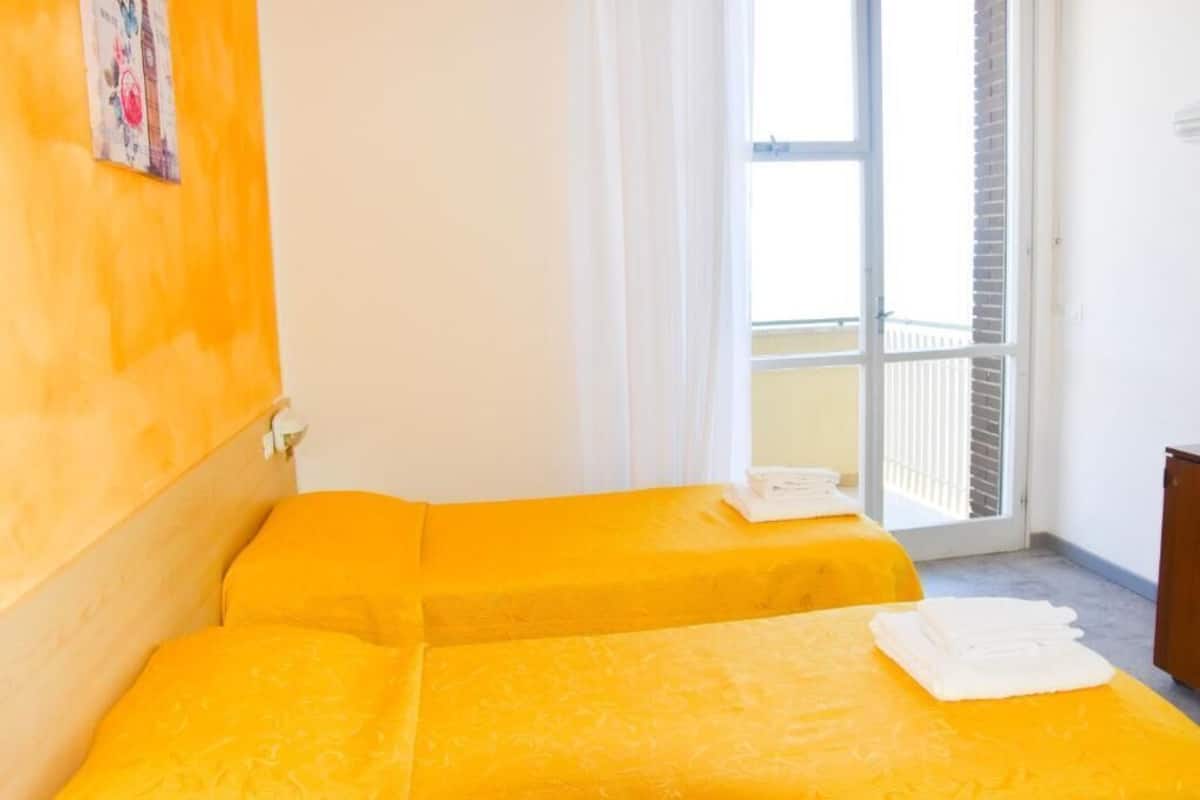 A room with two beds, a window with a view of a balcony, and a door leading outside.