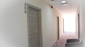 Un pasillo con una puerta marcada '208', una alfombra estampada y una silla.