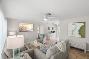 Ein modernes Wohnzimmer mit einer Couch, einem Couchtisch und einem Fernseher. Es gibt einen Essbereich mit Tisch und Stühlen.