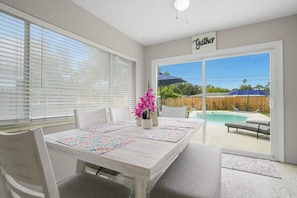 Ein Essbereich mit Tisch für vier Personen, einem Blumentopf und Blick auf einen Hinterhof mit Pool.