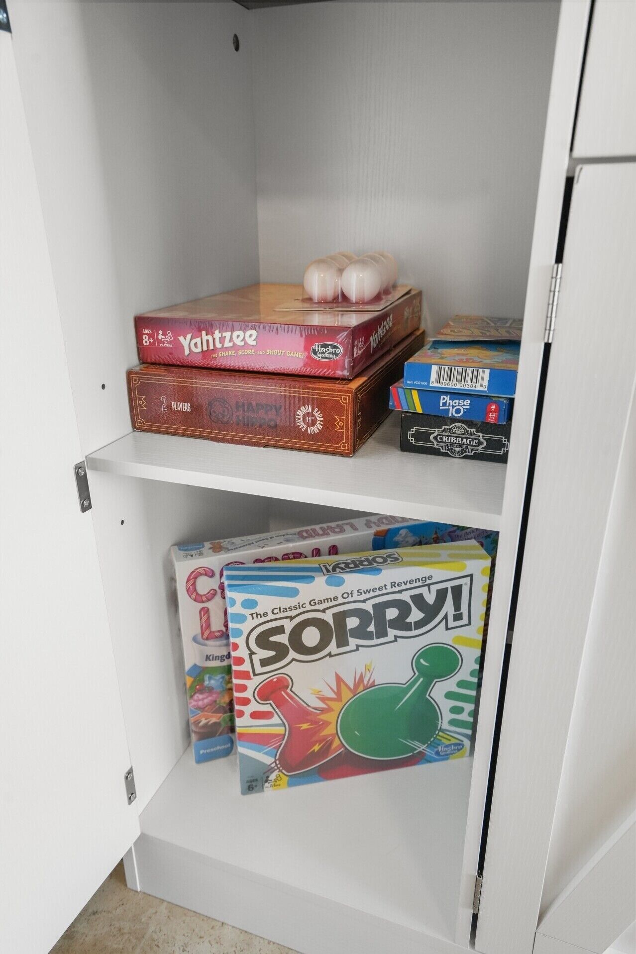 A cabinet with board games including Yahtzee, Hasbro, and Sorry!