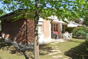 Ein Backsteinhaus mit überdachter Terrasse, einem Kinderwagen und Gartenmöbeln.